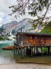 Naklejka premium Lago di Braies or Lake Braies crystal blue lake with wooden rowing boats in Italian Dolomites. Mountain forest lake in Italian alps Dolomites South Tyrol. Woden cabin hut and pontoon above the lake.