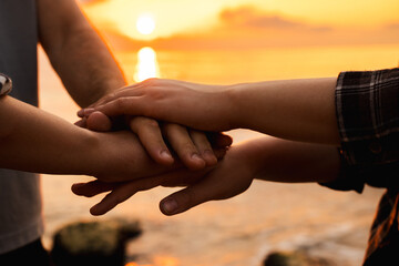 Close-up of three people joining hands in unity at sunrise on the beach, symbolizing teamwork, trust, and emotional connection