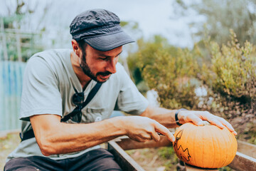 young man carving halloween pumpkin into jack-o'-lantern outdoors