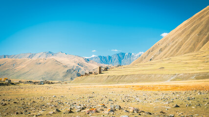 Panoramic view of Truso Valley in Georgia on a sunny autumn day. Golden grasslands and majestic Caucasus Mountains under a deep blue sky create a peaceful natural scene