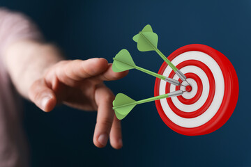 Hand reaching towards dartboard with darts in the center, representing business targets, goals, and...