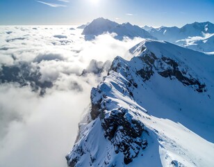 Aerial view of a snow-covered mountain ridge, with a layer of clouds below. Bright sunlight shining from above