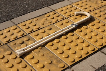 White cane resting on tactile paving, a symbol of accessibility and independence, perfect for projects about disability and urban design