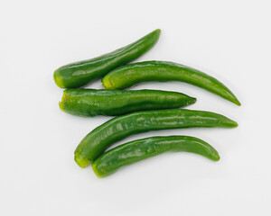 A group of fresh green chili peppers arranged on a clean white surface. Bright, glossy skins suggest crisp, flavorful ingredients ready to spice up sauces, salsas, stews, or healthy dishes