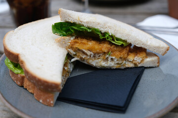 Sandwich with battered fish fingers and lettuce served on plate on wooden table. Selective focus.