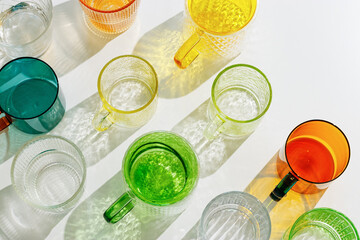 Colored shiny drink Glasses still life with shadow and sunlight reflections on white, minimal aesthetic top view summer photo, refraction at glass cups with sun flare, creative contemporary pattern