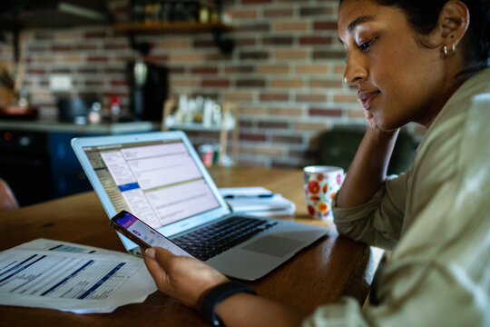 Woman using an banking app on her phone while going over her bills and finances