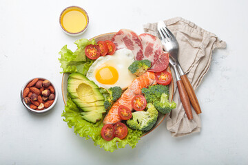 Healthy ketogenic diet concept showing a balanced meal on plate with salmon, avocado, fried egg, bacon, broccoli, tomato, and fresh salad, promoting low carb and high fat eating