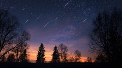 Night sky scene featuring a meteor shower streaking over silhouetted trees with a colorful sunrise glow