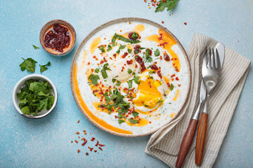 Turkish eggs cilbir, a delicious and colorful breakfast with poached eggs on yogurt, seasoned with spices and fresh herbs, arranged on a blue background