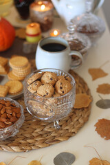 Lit candles, cookies, chocolate, nuts, tea, wine, pumpkins, books, reading glasses and autumn leaves on the table. Autumnal hygge at home. Selective focus.