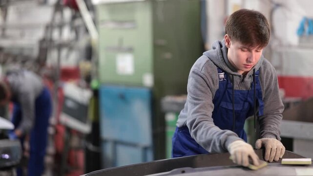 Guy worker removes dents on cars exterior, restores vehicle to its original form. Male auto mechanic polishes bumper, eliminating deformations, hiding flaws 