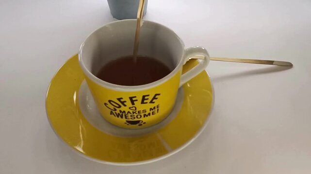 A warm cup of coffee being poured into a yellow mug with the word coffee on it