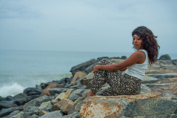 A woman sits on a rock by the ocean, looking out at the water