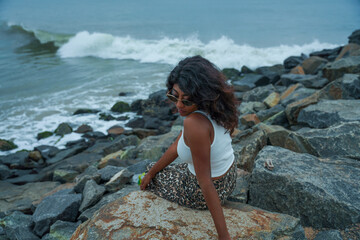 A woman is sitting on a rock by the ocean