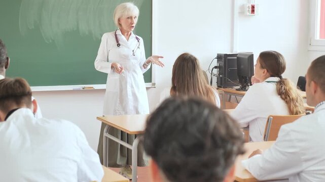 Senior woman professor explaining subject to group of medical students and colleagues in university.