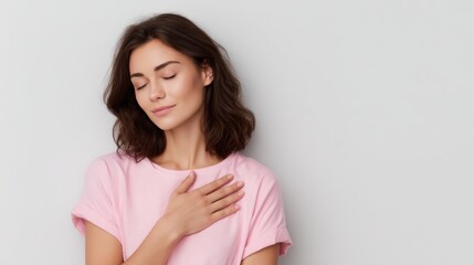 Fototapeta premium Serene brunette woman in pink t-shirt, eyes closed, hands over heart, expressing gratitude and calm emotion, isolated on white background
