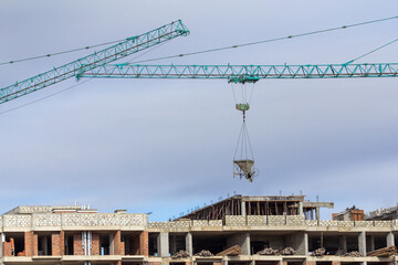 Tower crane transporting concrete skip bucket above a multi-story construction site, building materials transfer, urban housing development progress