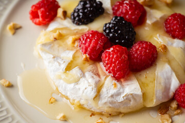 Melted camembert cheese topped with raspberries, blackberries, walnuts and honey. Healthy dessert. Shallow depth of field.