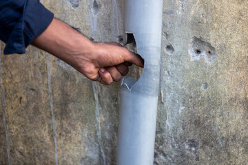 Hand pointing to a damaged pipe attached to a concrete wall