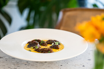 Gourmet dish with morel mushrooms on vibrant yellow sauce, garnished with herbs, served on white plate in elegant dining setting with floral accents.
