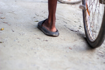 Closeup of a persons foot wearing a worn sandal next to a bicycle wheel