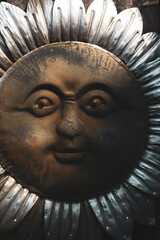 Close-up of rustic metal sun face sculpture with weathered texture. Vintage metallic sun wall art with expressive facial features.