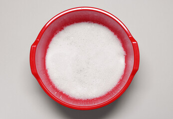 Red plastic basin with water and foam on grey background, top view