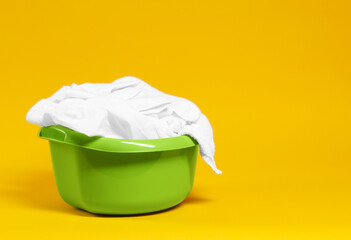 Plastic basin with laundry on yellow background. Space for text