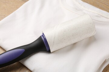 Sticky lint roller and shirt on wooden table, closeup