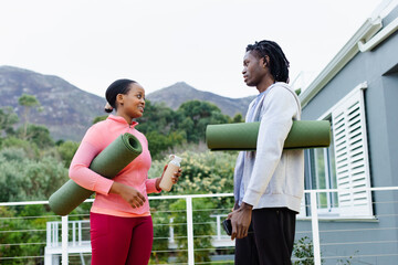 African American friends standing on balcony carrying yoga mats with water bottle and smartphone