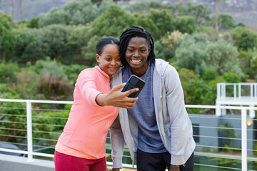Naklejka premium African American friends taking selfie on terrace overlooking garden in sportswear with smartphone
