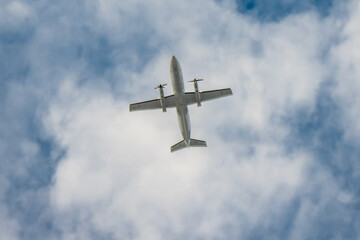 A twin-engine plane flying in a blue sky between clouds. Transportation.