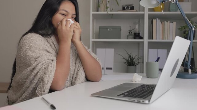 Sick woman working from home sneezing at her desk