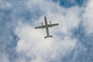 A twin-engine plane flying in a blue sky between clouds. Transportation.