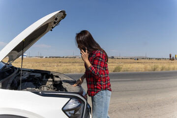  woman is talking on phone while looking at her car's engine with the hood open