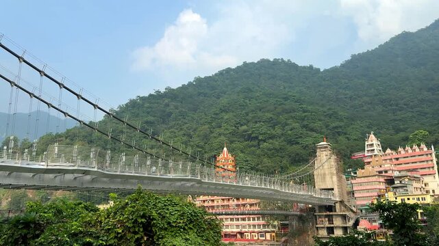 New suspension Laxman Jhula bridge over the Ganges river with Hindu temples and lush green mountains in Rishikesh, India