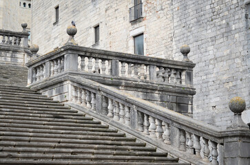 Grand stone staircase with ornate balustrades and spherical finials leading to a historic building. A pigeon perches on a post; the architecture suggests classical European design.