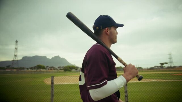 Young baseball player in uniform walking on the field, bat on shoulder, ready for the game. Focus and determination before the first pitch. - Powered by Adobe