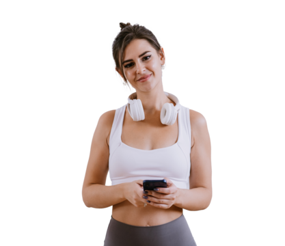 Attractive brunette American girl in sportswear and headphones on neck holds phone looks at camera smiles standing on transparent background