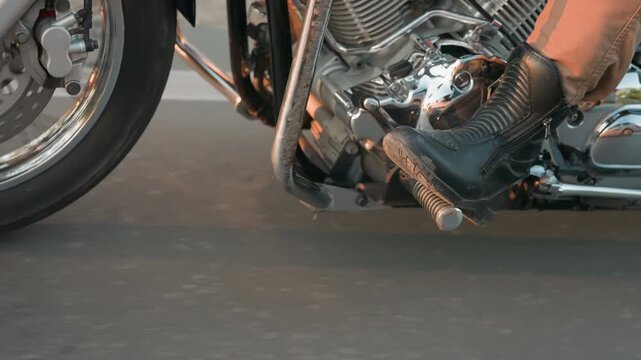 Leg view of rider and passenger on motorcycle footrests while traveling on asphalt road, showcasing leather boots, chrome engine details, and motion blur that conveys speed