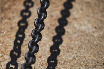 Close-up of dark metal chain casting shadow on concrete. Industrial chain with strong sunlight and sharp shadow.