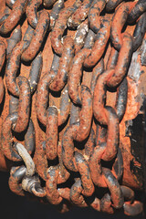 Close-up of heavy rusted metal chains in sunlight. Corroded industrial steel links with rough texture.