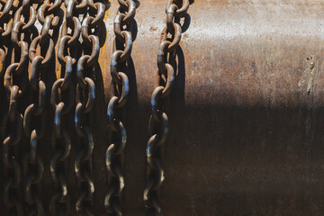Rusty industrial chains hanging in sunlight. Weathered metal chains on corroded steel surface.