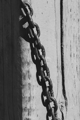 Rusted metal chain lying on weathered wooden surface. Old industrial chain casting shadow on faded paint.