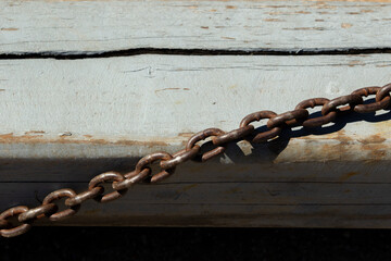 Rusted metal chain lying on weathered wooden surface. Old industrial chain casting shadow on faded paint.