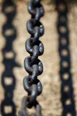 Close-up of dark metal chain casting shadow on concrete. Industrial chain with strong sunlight and sharp shadow.