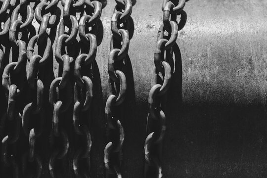 Rusty industrial chains hanging in sunlight. Weathered metal chains on corroded steel surface.