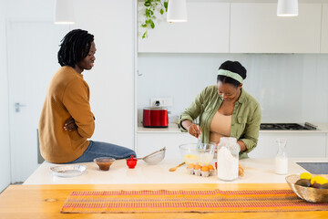 African American couple sitting at island mixing batter in glass bowl and sifting flour in kitchen