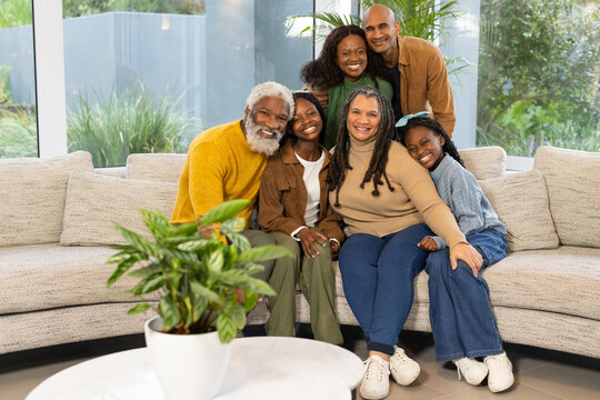 African American family gathering on beige sectional sofa in living room by large windows - Powered by Adobe